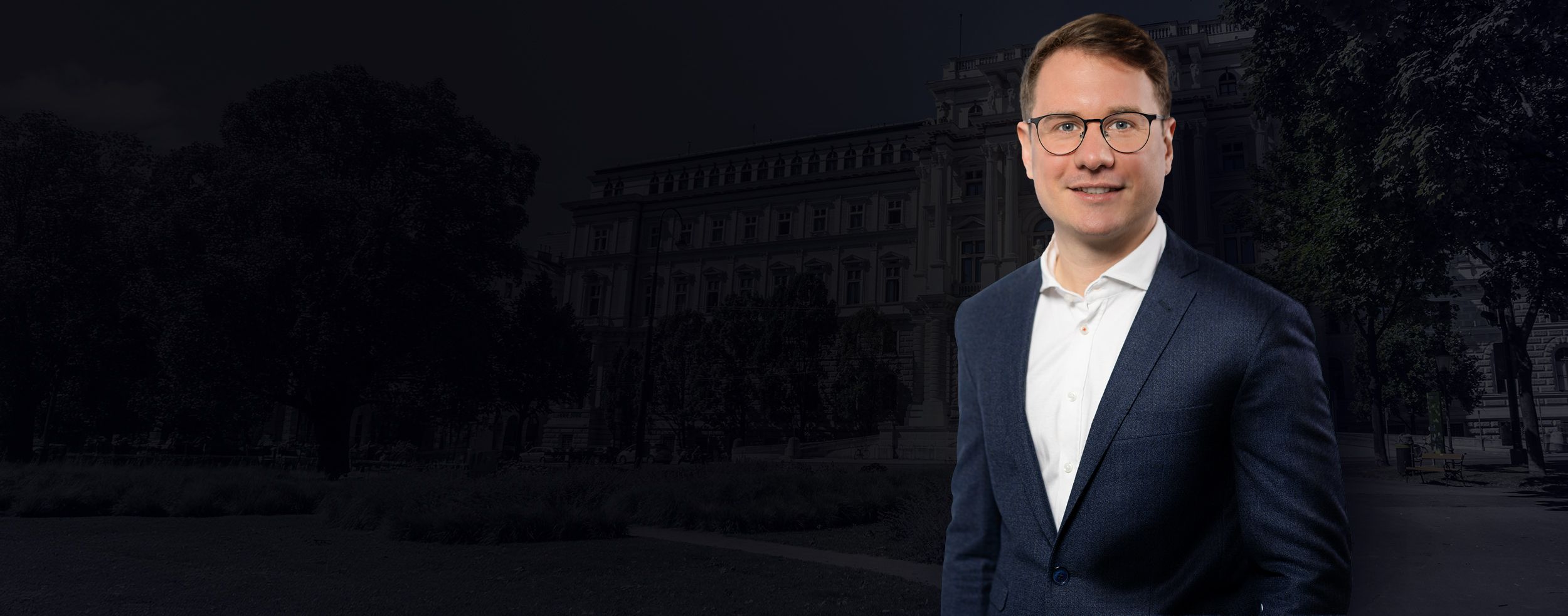 Mag. Laurenz Villani in dunklem Anzug und weißem Hemd vor einem weißem Justizgebäude, was mit einer Fläche darüber abgedunkelt ist